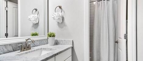 A bathroom with a marble sink, a mirror, a potted plant, and a shower curtain.