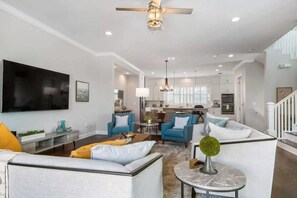 A spacious living area with a flat-screen TV, sofas, a coffee table, and a ceiling fan.