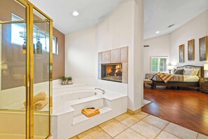A modern bathroom with a large bathtub, a glass shower enclosure, and a fireplace.