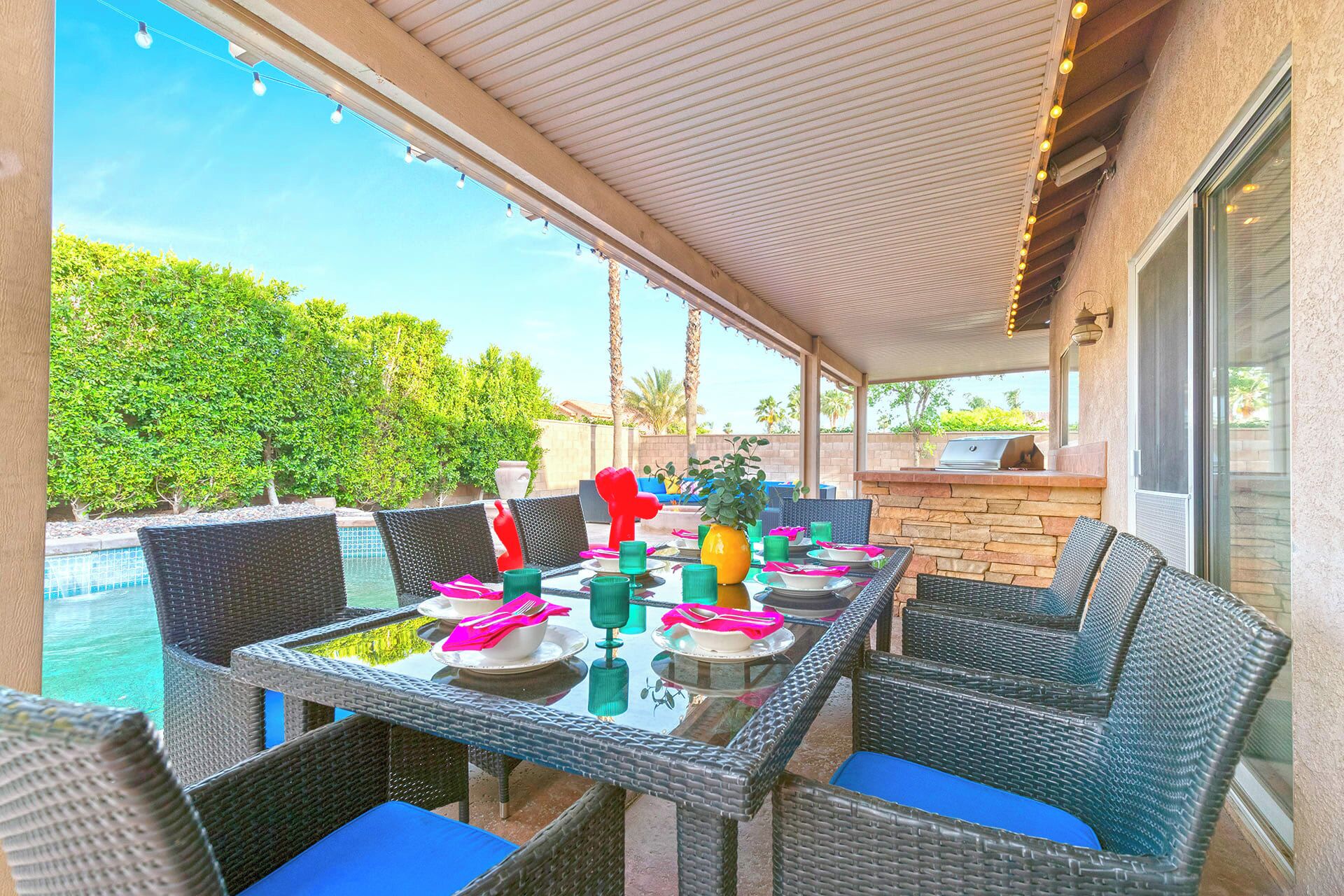 Un patio exterior con mobiliario de mimbre, una piscina y una zona de barbacoa.
