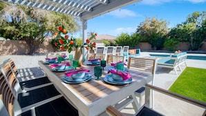 Un'area pranzo all'aperto con una pergola, una piscina e un prato curato.