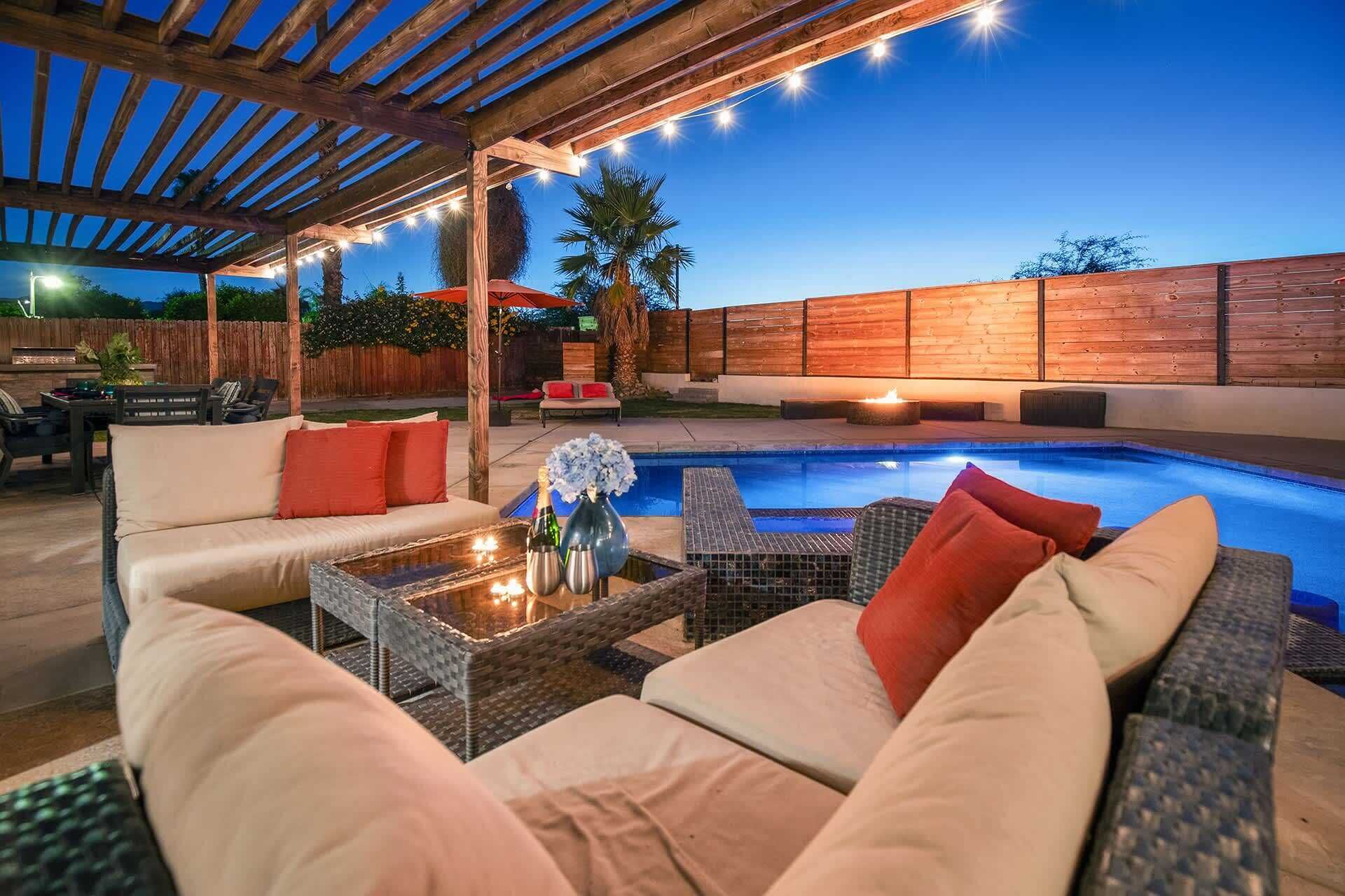 An outdoor patio with a pool, wicker furniture, and string lights.