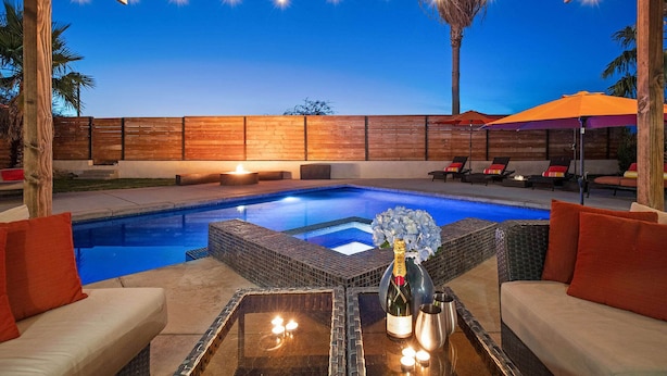 A pool area with a pergola overhead, lounge chairs, and a table with a bottle of champagne.