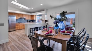 A modern kitchen with wooden cabinets, a stainless steel refrigerator, and a dining area with a wooden table set for four.