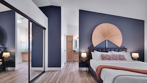 A modern bedroom with a large bed, a wall-mounted fan, and a sliding glass door leading to a bathroom.