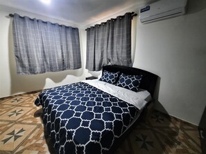 A bedroom with a bed, curtains, an air conditioning unit, and patterned flooring. - Beautiful 3 bedroom house - Depot House Villa (Osu - Accra)