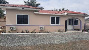 Una casa de dos pisos con techo rojo, dos ventanas y un equipo de aire acondicionado al costado.