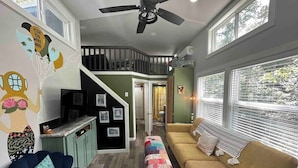 A spacious living area with a sofa, a blue chair, a kitchen area, and a staircase leading to an upper level. - Waterfall Cottage | Hot Tub, Game Room, Fireplace (Mentone)