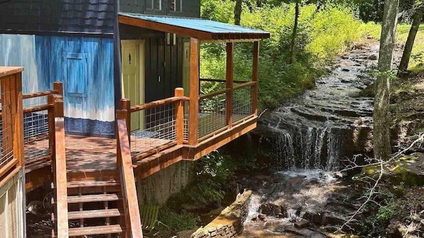 A rustic cabin with a wooden deck and a small waterfall. - Waterfall Cottage | Hot Tub, Game Room, Fireplace (Mentone)