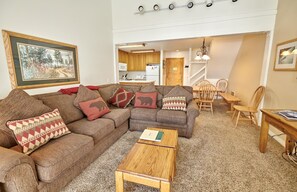 A cozy living room with a sectional sofa, a wooden coffee table, and a dining area with wooden chairs and a table. - St. Anton Wooded View 2-Bedroom Condos w/ Ski Lockers (Mammoth Lakes)