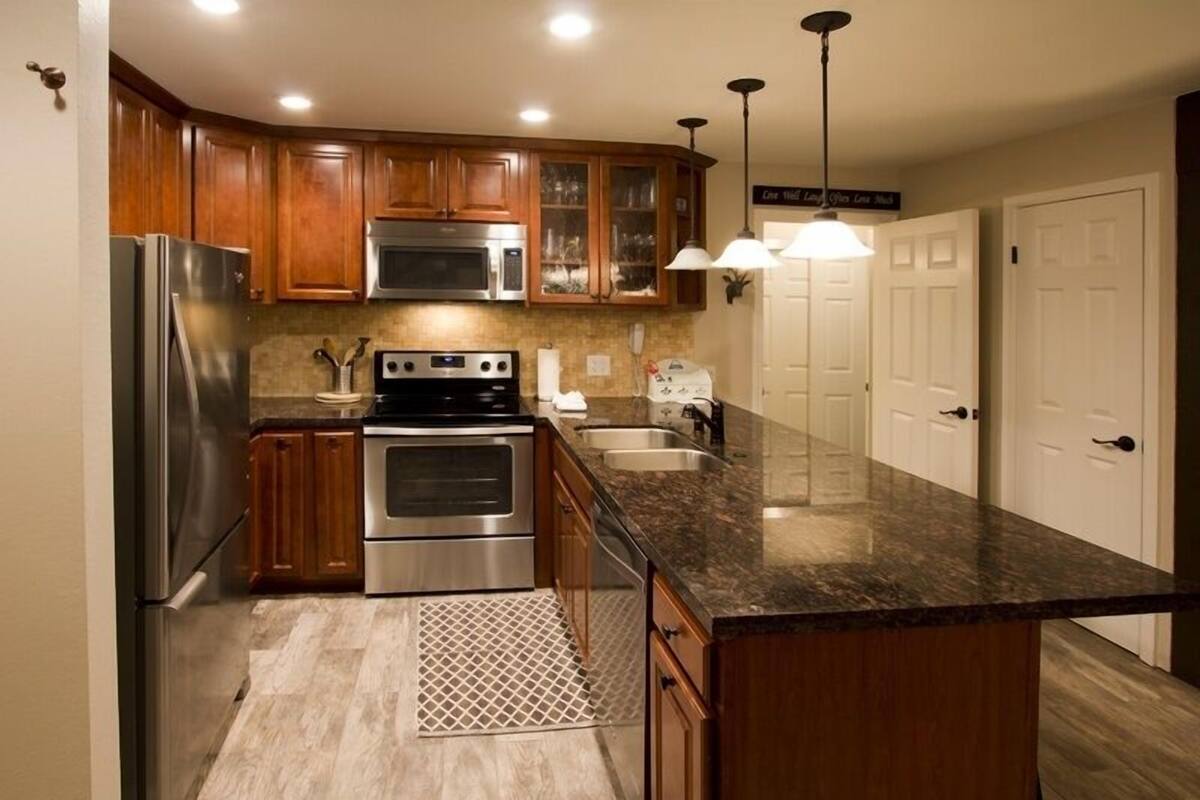 A modern kitchen with wooden cabinets, stainless steel appliances, granite countertops, and pendant lighting.