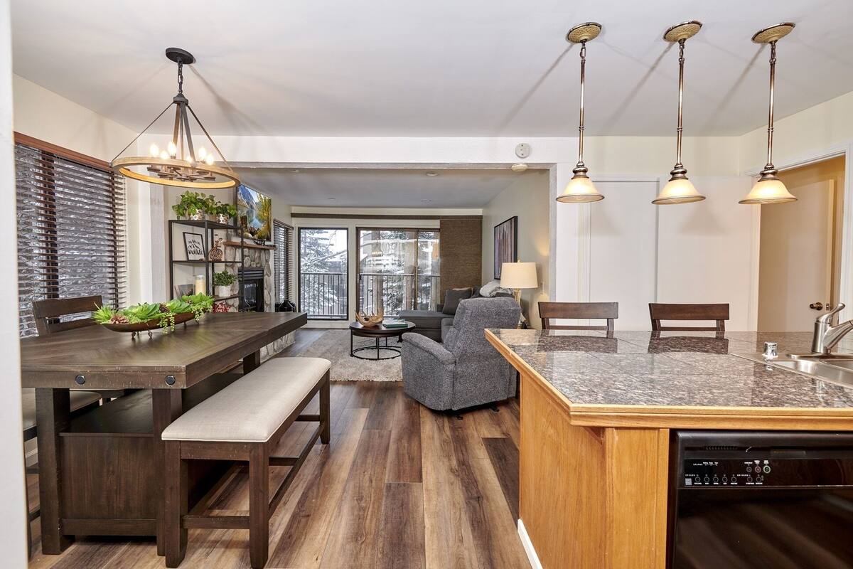 A modern kitchen with a central island, wooden flooring, and pendant lighting.