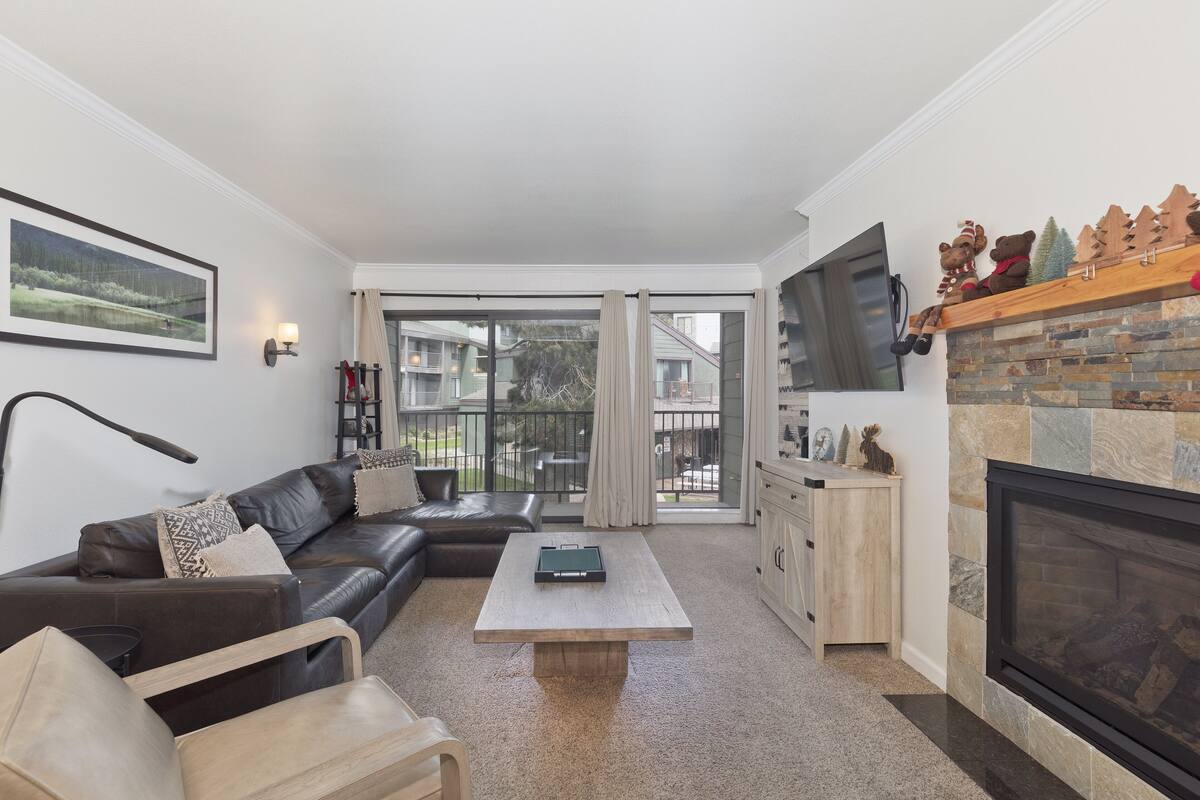A modern living room with a leather sofa, a wooden coffee table, a fireplace, and a large TV.
