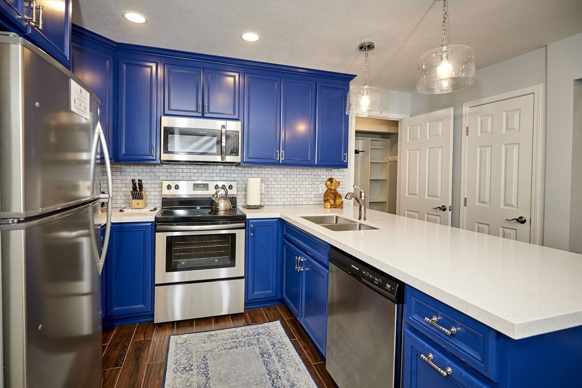 A modern kitchen with blue cabinets, stainless steel appliances, and a white countertop.
