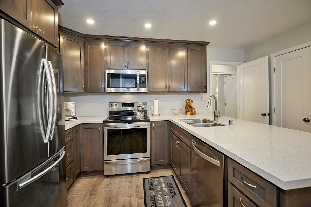 A modern kitchen with stainless steel appliances, wooden cabinets, and a white countertop.