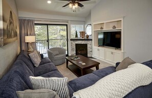 A living room with a sofa, coffee table, fireplace, TV, and a balcony with curtains.