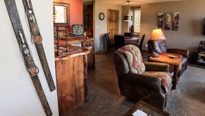 Ein gemütliches Wohnzimmer mit einer Holztrennwand, einem Ledersessel und einer rustikalen Einrichtung, darunter Ski und eine Vogelstatue.