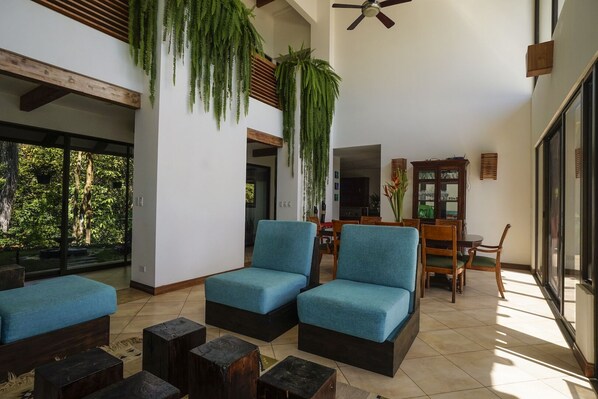 A spacious living area with a large window, a ceiling fan, and a dining area with wooden furniture.
