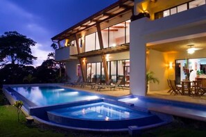 A modern hotel with a large outdoor swimming pool, a covered patio area, and a well-lit interior.