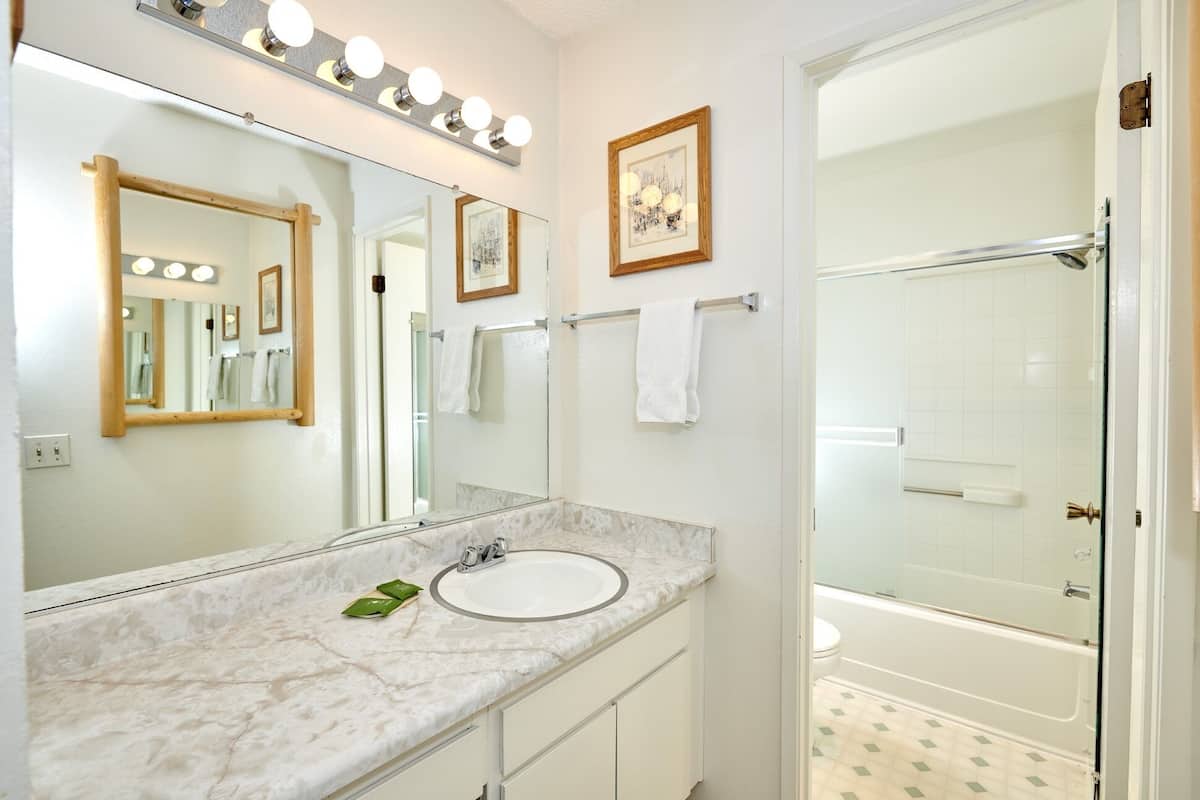 A bathroom with a large mirror, vanity with a sink, and a shower area.