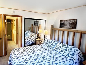 Ein Schlafzimmer mit einem Bett, Nachttischlampen, einem Spiegel und einem gerahmten Bild an der Wand.