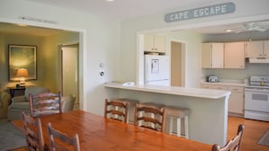 A dining area with a wooden table and chairs, a kitchen with white cabinets, and a ceiling fan. - Lovely three bedroom home located in desirable West Dennis neighborhood! (West Dennis)