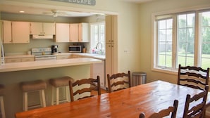 A kitchen with a wooden table and chairs, a ceiling fan, and a sign that reads "CAPE ESCAPE". - Lovely three bedroom home located in desirable West Dennis neighborhood! (West Dennis)