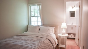 A bedroom with a bed, a nightstand, a lamp, and a bathroom visible through an open door. - Lovely three bedroom home located in desirable West Dennis neighborhood! (West Dennis)