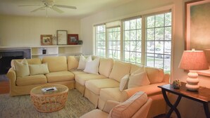A living room with a sectional sofa, a glass coffee table, a fireplace, and large windows with a view of the outdoors. - Lovely three bedroom home located in desirable West Dennis neighborhood! (West Dennis)