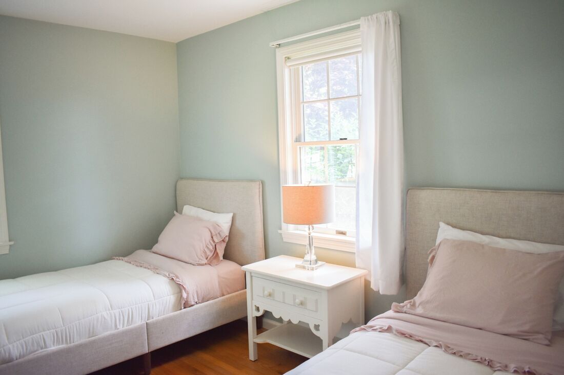 Un dormitorio con dos camas individuales, una mesita de noche con lámpara y una ventana con cortinas.