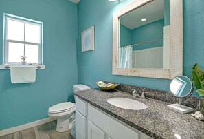 Un baño con inodoro blanco, un lavabo con encimera de granito, un espejo grande y una ventana.