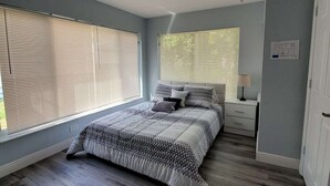 A bedroom with a large bed, a nightstand, a lamp, and a window with blinds. - Great house on close to two acres with fishing pond (Oklahoma City)