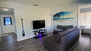 A modern living room with a large gray sofa, a flat-screen TV on a stand, and a wall-mounted painting of a beach scene. - Great house on close to two acres with fishing pond (Oklahoma City)
