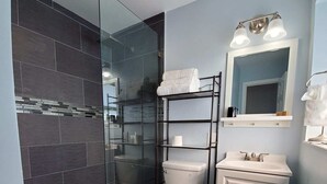 A modern bathroom with a glass shower enclosure, a white toilet, a sink with a mirror, and a towel rack. - Great house on close to two acres with fishing pond (Oklahoma City)