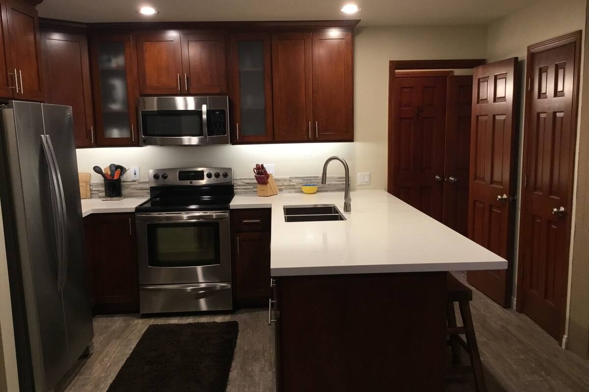 A modern kitchen with stainless steel appliances, wooden cabinets, and a white countertop.