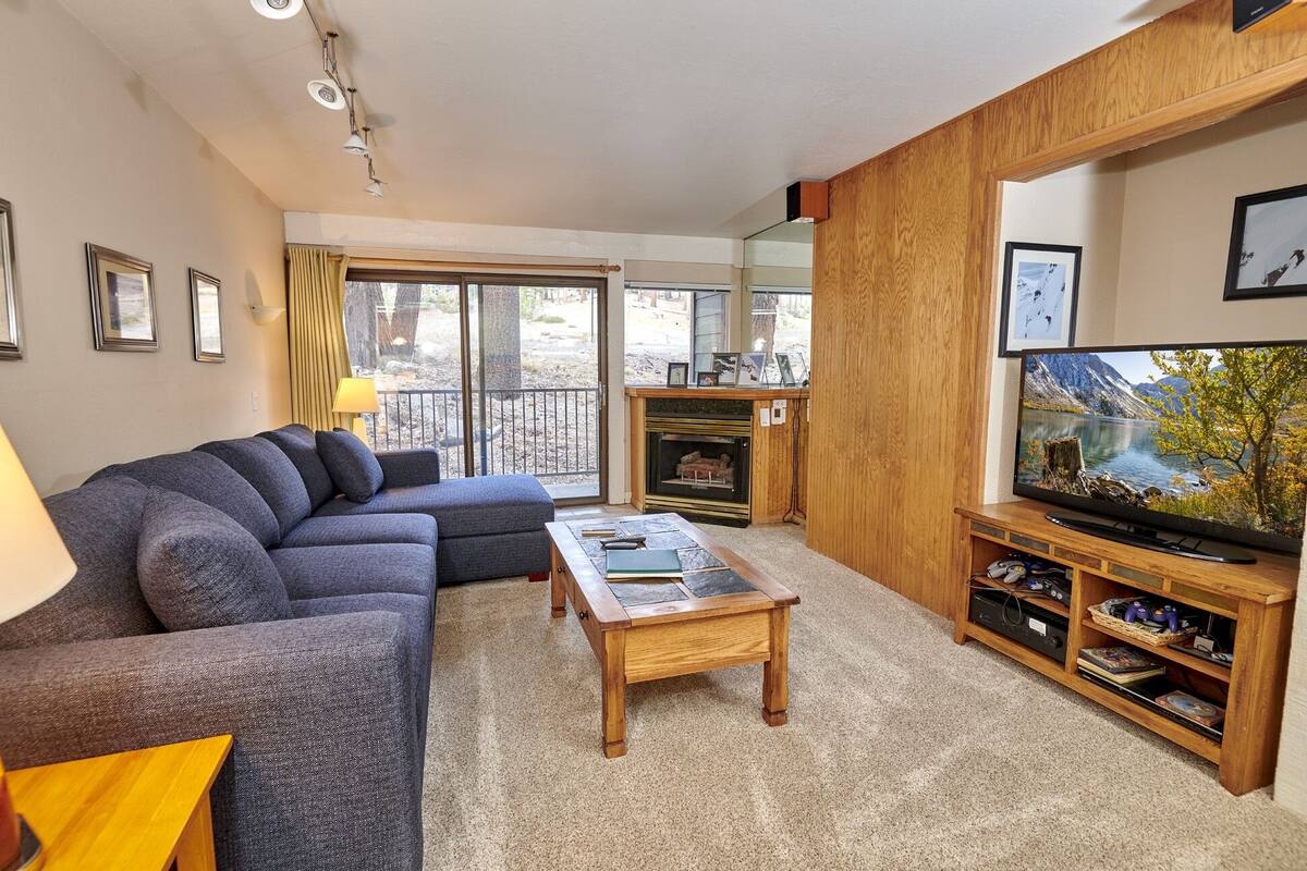 A living room with a sectional sofa, a coffee table, a fireplace, a television, and a balcony with a view.