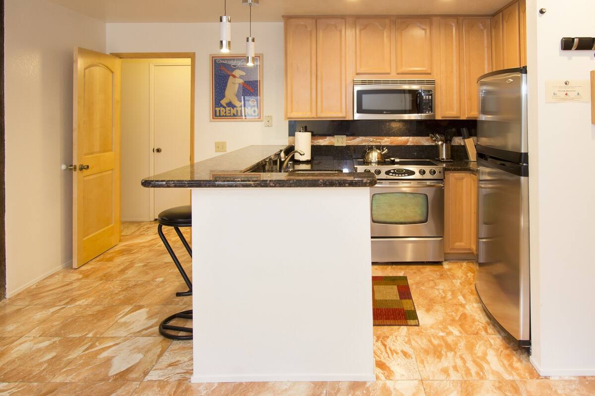 A kitchen with wooden cabinets, a stainless steel refrigerator, a microwave, an oven, and a granite countertop.