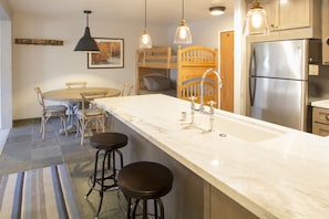 A kitchen with a large island, bar stools, a dining table with chairs, a bunk bed, and a refrigerator.