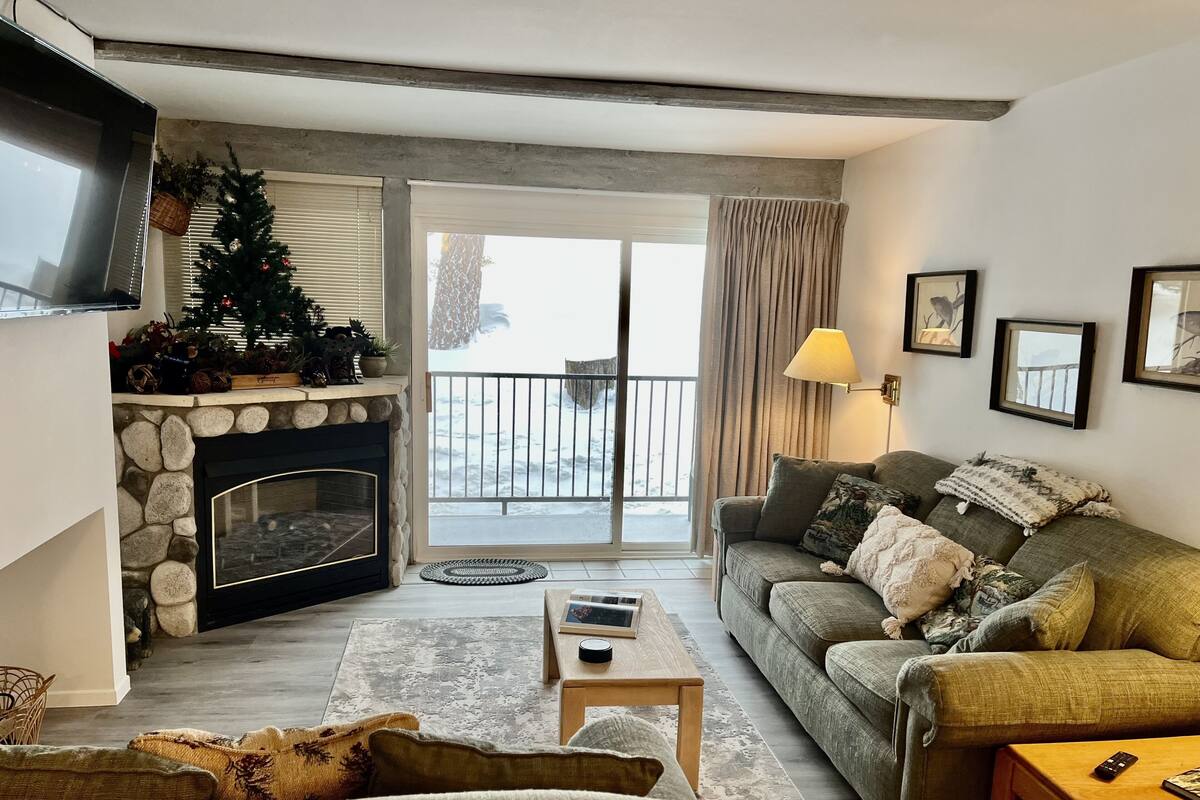A living room with a stone fireplace, a green sofa, a wooden coffee table, and a television mounted on the wall.
