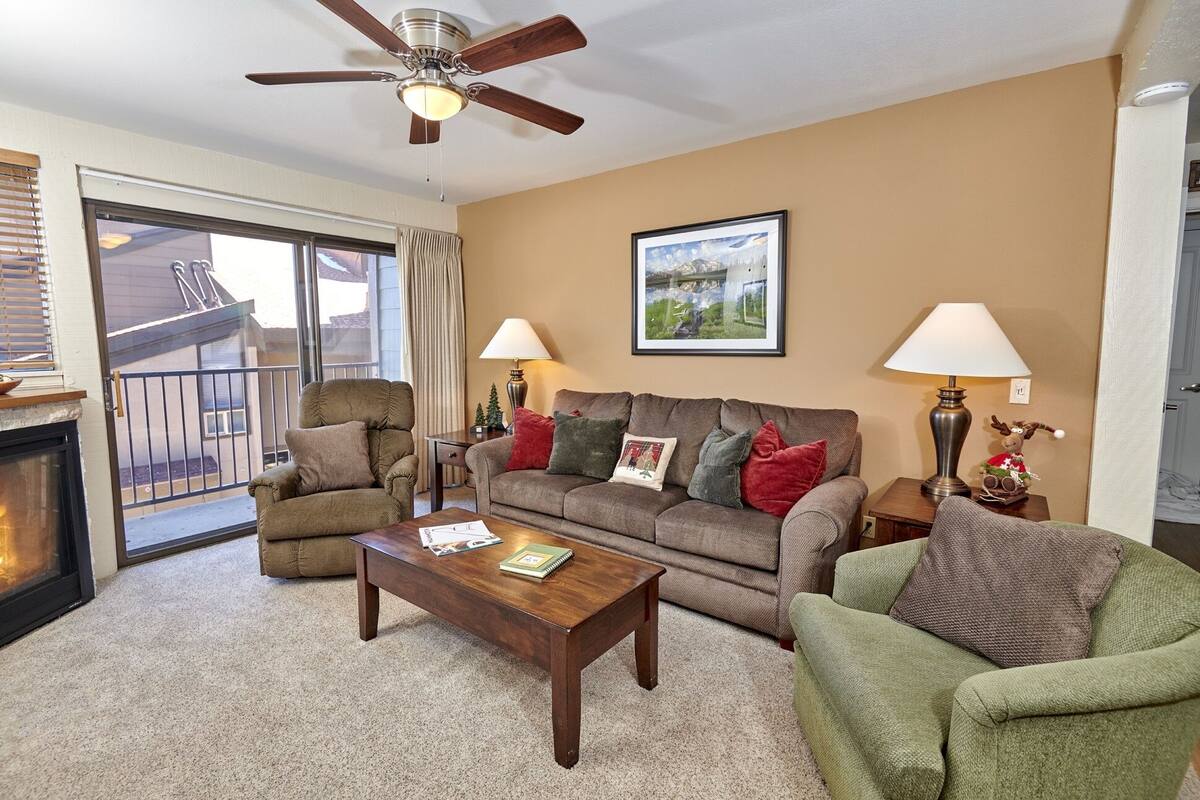 A living room with a fireplace, a ceiling fan, a sofa, a coffee table, and two lamps.