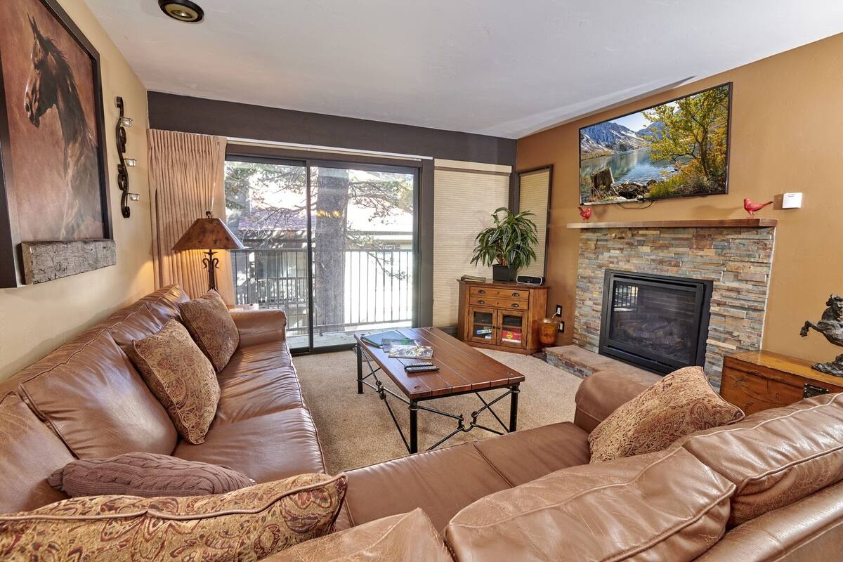 A living room with a leather sofa, a fireplace, a large window, and a balcony.