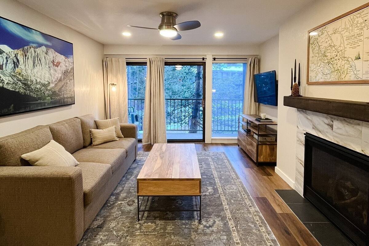 A living room with a sofa, coffee table, fireplace, and a large window with curtains.