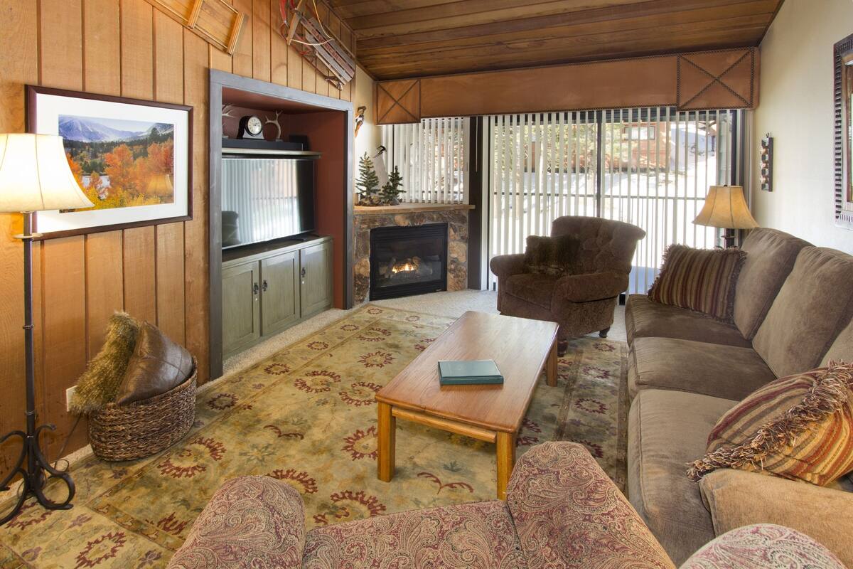 A cozy living room with a fireplace, a sofa, a coffee table, and a patterned rug.