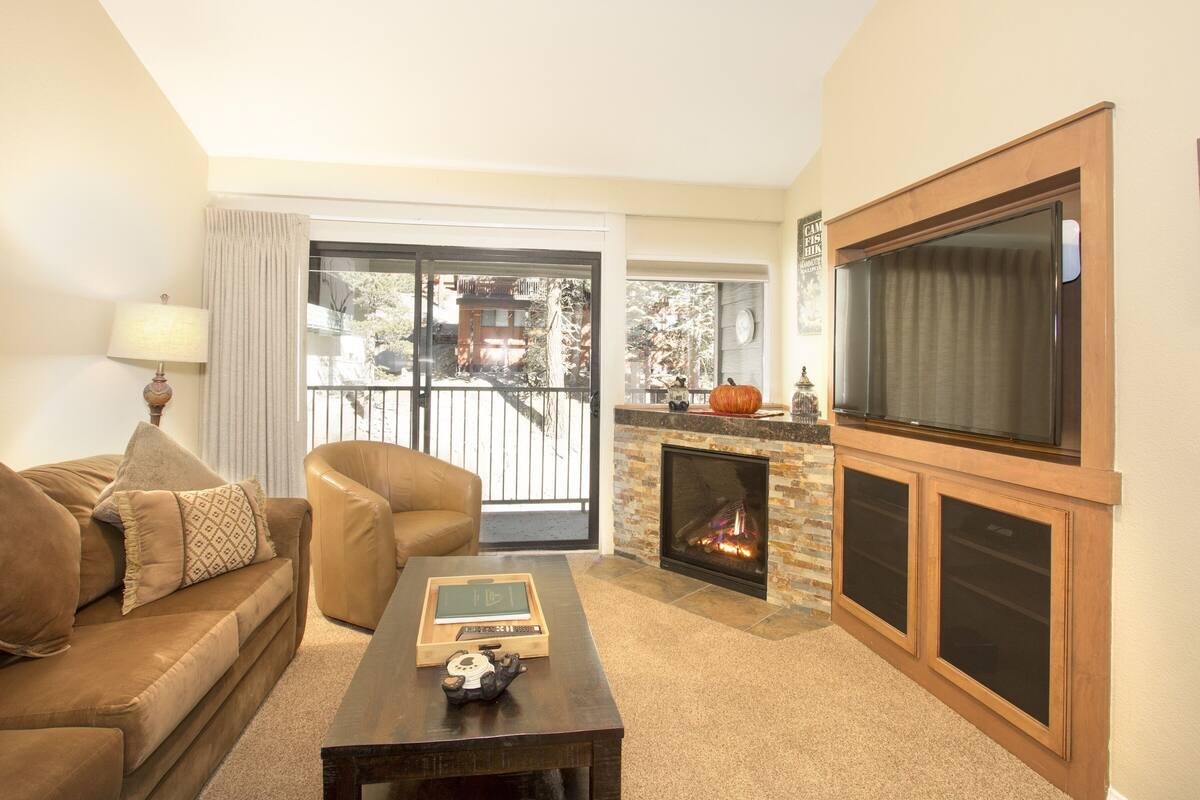 A living room with a sofa, armchair, coffee table, fireplace, and large TV.
