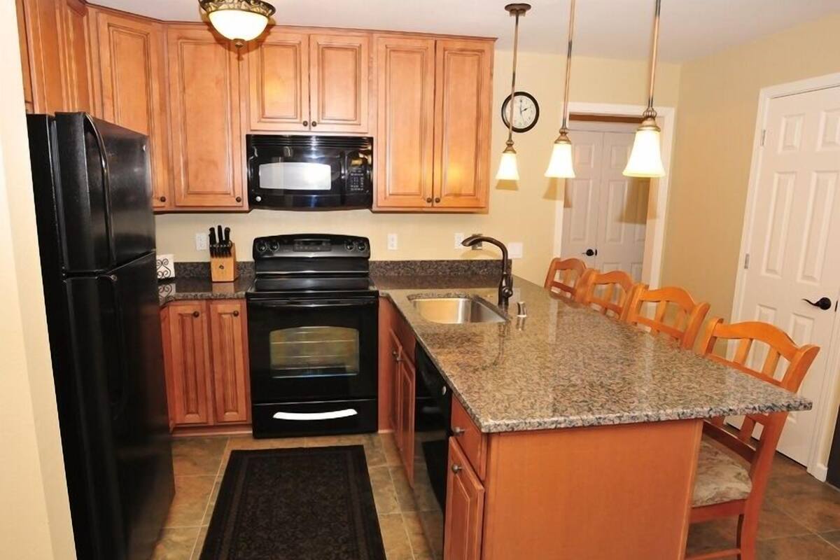 A kitchen with wooden cabinets, a black refrigerator, a microwave, a stove, and a granite countertop.