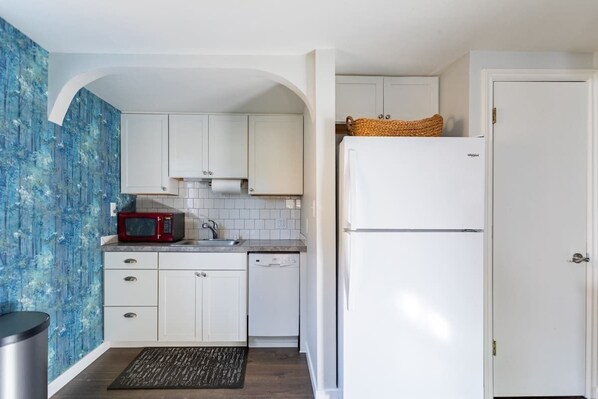 Una cocina compacta con armarios blancos, un microondas rojo y un refrigerador blanco.