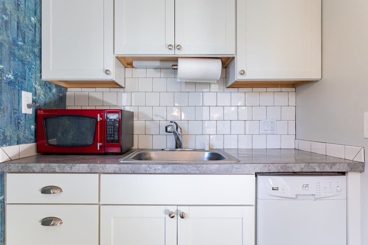 Una cucina con mobili bianchi, un forno a microonde rosso, un lavello in acciaio inossidabile e una lavastoviglie.