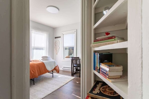 A bedroom with a bed, a chair, a bookshelf, and a window.