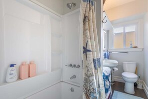 A bathroom with a bathtub, shower curtain, sink, toilet, and a window.