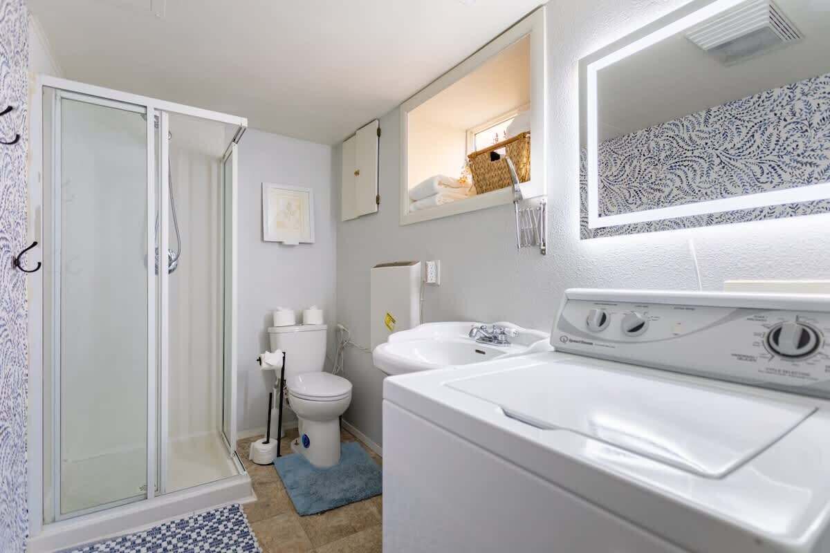 A bathroom with a glass shower enclosure, a toilet, a sink, and a washing machine.